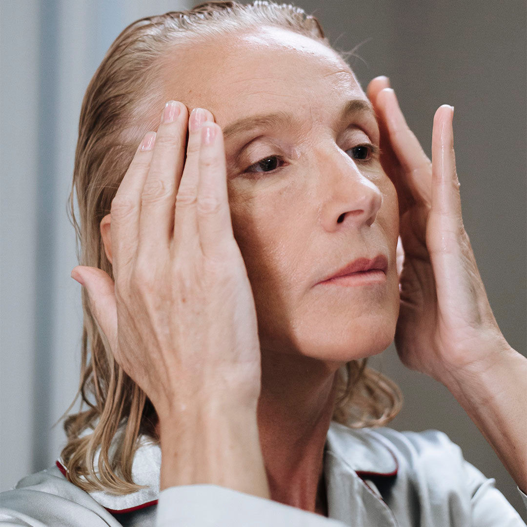 an older woman massaging her face in her pajamas