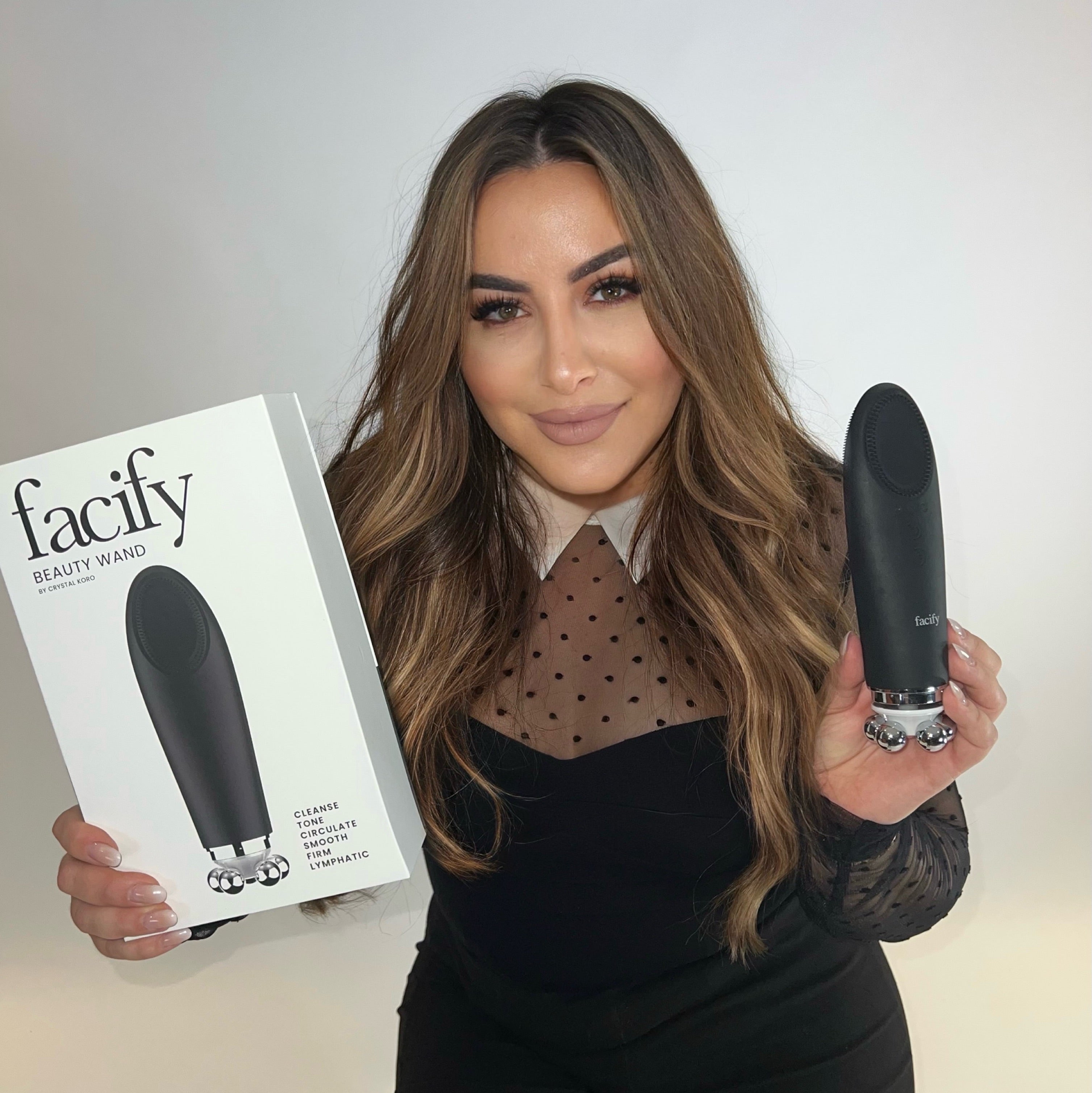 crystal koro founder of the facify beauty wand device holding up the product packaging and wand smiling