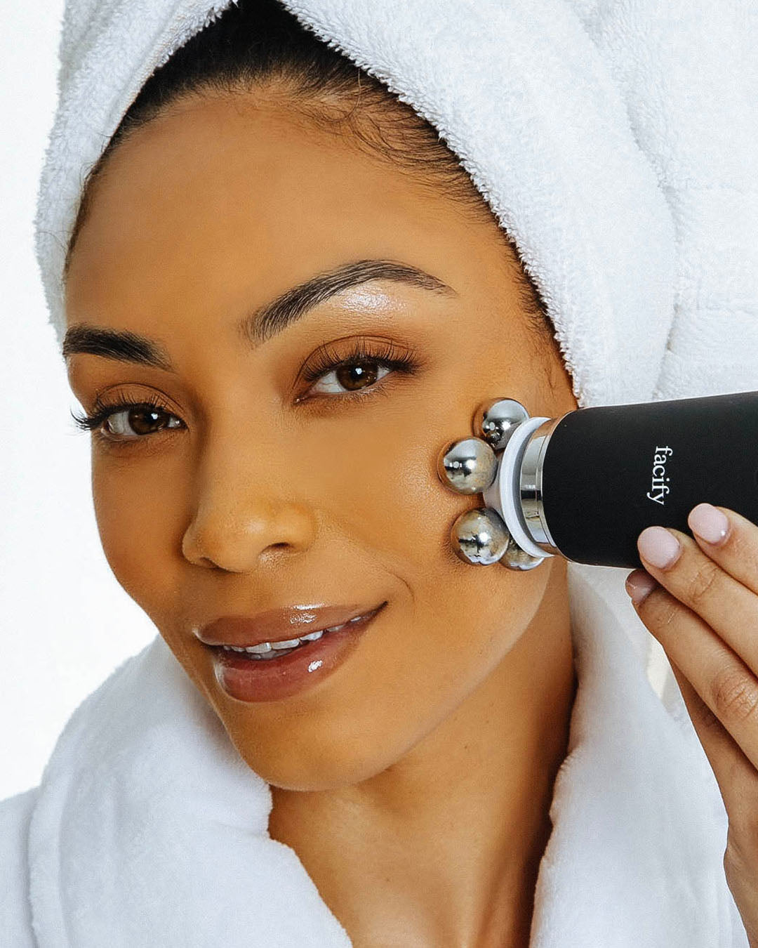 woman in spa robe and headband using the lymphatic massage attachment attachment facify beauty wand device on her face