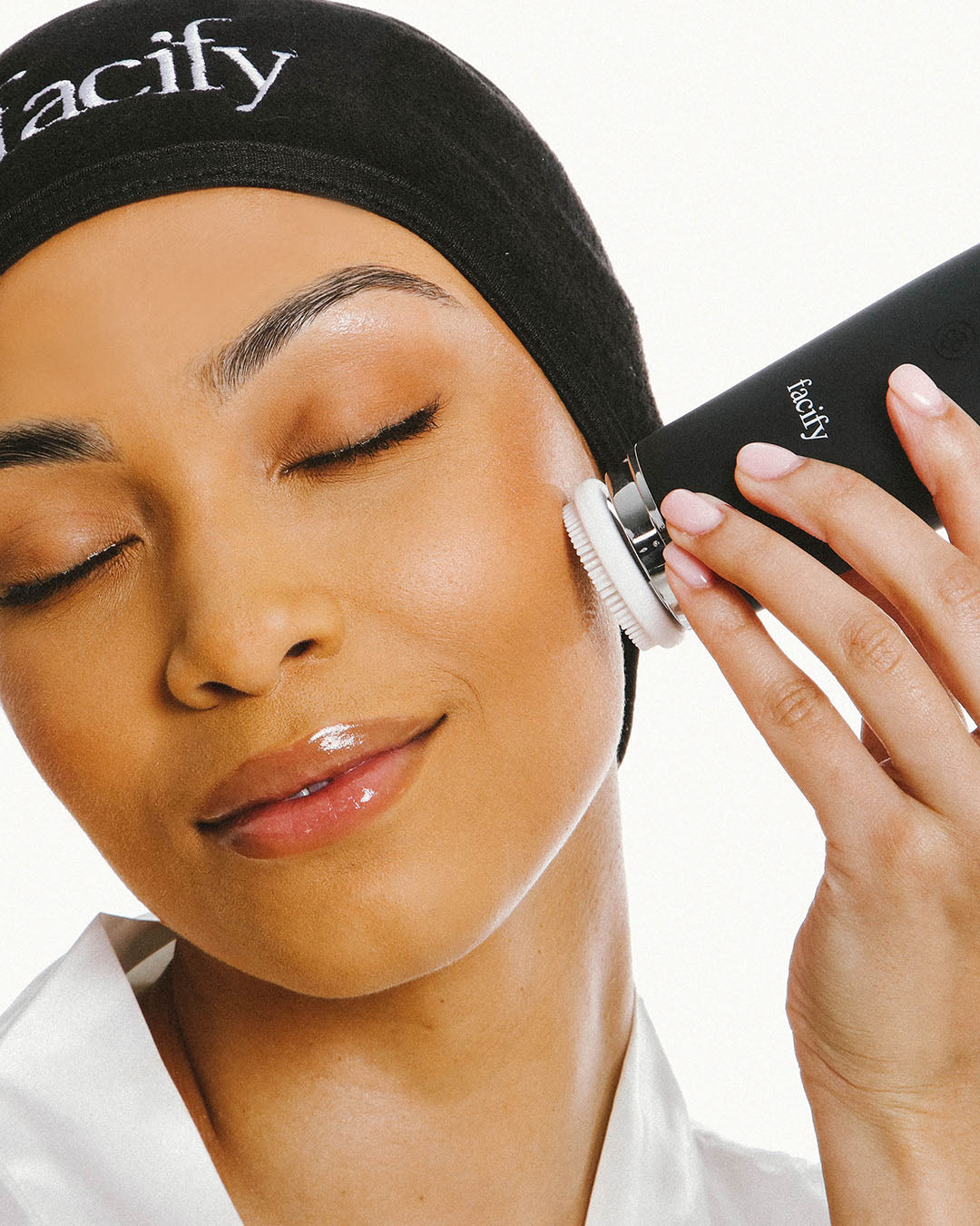 woman in spa robe and headband using the large cleansing head attachment facify beauty wand device on her face