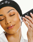 woman in spa robe and headband using the large cleansing head attachment facify beauty wand device on her face